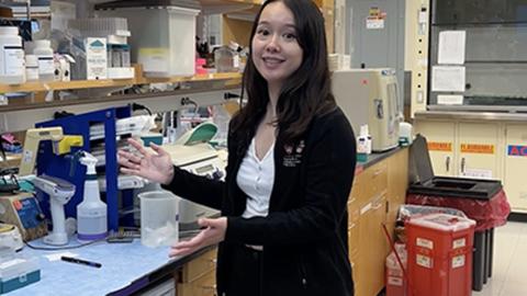 A young scientist gestures towards her lab bench.