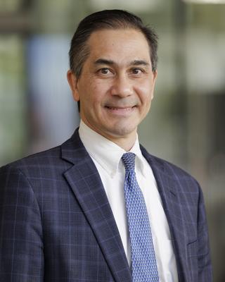 Man in a blue suit jacket and tie smiles at the camera