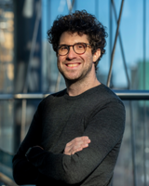 Person with dark curly hair and glasses smiling at the camera