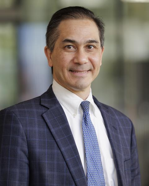 Man in a blue suit jacket and tie smiles at the camera