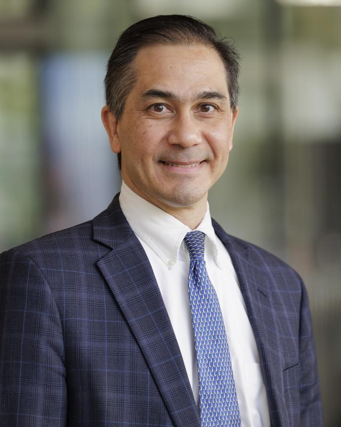 Man in a blue suit jacket and tie smiles at the camera
